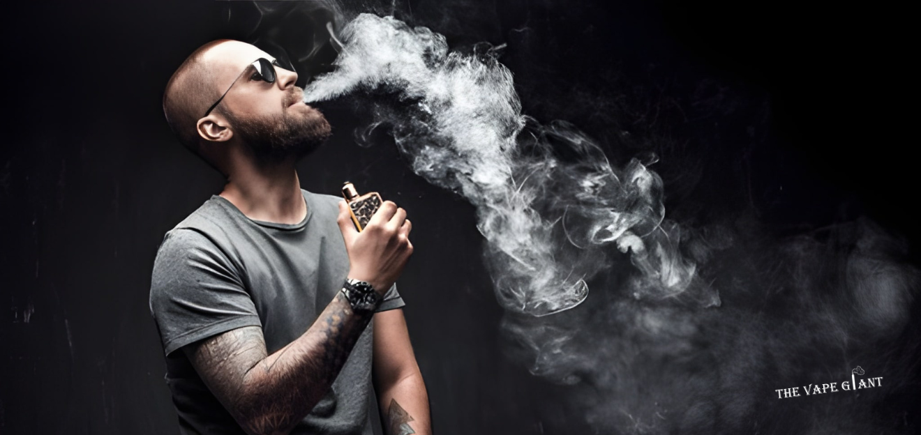 Man with a beard and sunglasses exhales a large cloud of vapor against a dark background, holding a vape device. The mood is relaxed and contemplative.